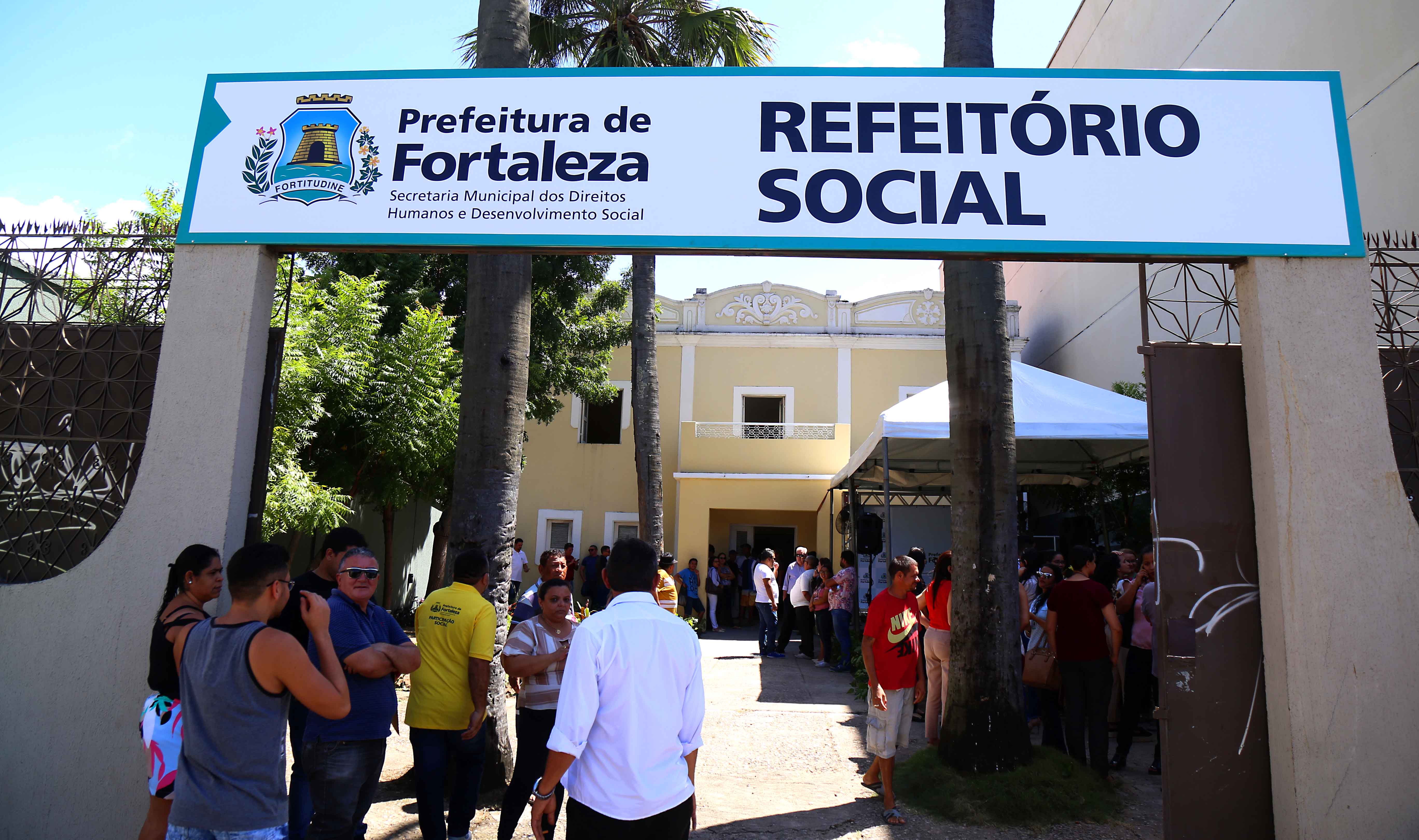 fachada do refeitório social com placa e pessoas na porta